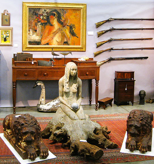 Fronting the spacious display of Blandon Cherry of Paris, Kentucky, was this eye-catching 1960s sculpture of a woman emerging from a carved cedar tree trunk—not a mermaid but perhaps a dryad—priced at $4500. The pair of cast-iron lions from Louisville, Kentucky, was $12,500. They might be better off in a garden. At the back of the scene, the cherry and mahogany-veneer southern sideboard/sugar chest, South Carolina, Kentucky, or Middle Tennessee, was $8900. It was below a 1959 painting by Bernard Cathelin (French, 1919-2004), priced at $8500. 