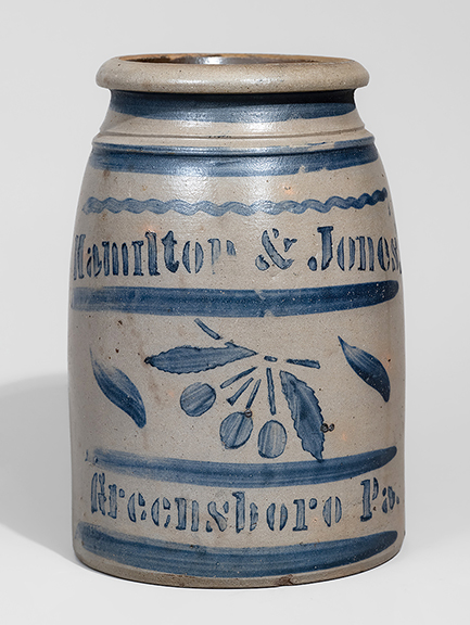 This western Pennsylvania, circa 1870, stoneware canning jar, 9 3/8&rdquo; tall, with cobalt freehand and stenciled cherry decoration, stenciled &ldquo;Hamilton & Jones. / Greensboro Pa.,&rdquo; sold for $7800 (est. $2500/3500).