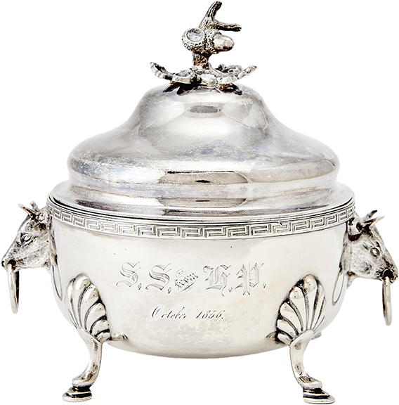 The silver butter dish, 1850s, has a circular body, a pierced liner, loose ring handles with cow masks, and hoof feet. The cover has an acorn and oak leaf finial. The dish brought $1536 (est. $400/600). It came from Jones, Shreve, Brown & Co., which operated in Boston, Massachusetts.