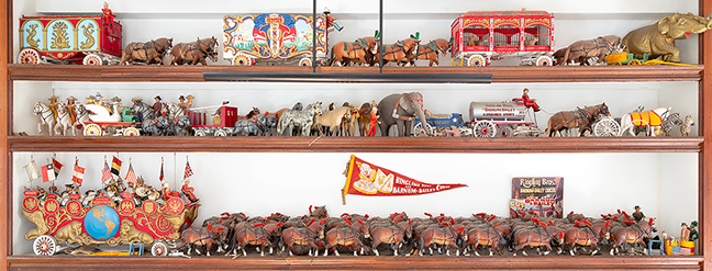 Carved and painted wood Ringling Brothers and Barnum & Bailey toy circus, 1970s, from an Upper East Side Manhattan estate, including a cage wagon with lions, a bandwagon with approximately 21 musicians, a team of approximately 48 horses, 9 horses and riders, an Uncle Sam figure, a “Police Patrol” wagon, magician figures, circus barrels, a swan-form wagon, camels, elephants, dogs, horses, acrobats, 5 zebras, a gold-painted elephant with an acrobat, and a felt pennant, approximately 100 pieces, sold for $15,360 (est. $3000/5000).