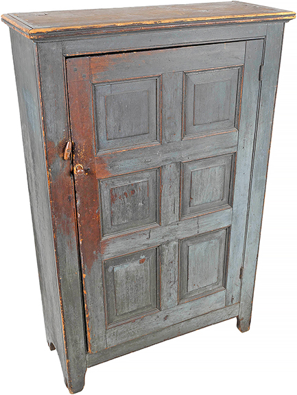 A Pennsylvania painted pine cupboard, possibly from Bucks County, circa 1820, retains much of its blue paint, revealing traces of a deep red-brown stain beneath. Below a molded cornice, the paneled door opens to three shelves. Measuring 54½