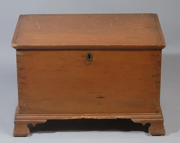The diminutive antique blanket chest appears to be constructed of pine. The case is finely dovetailed, and the lid has an applied molded edge. The chest is raised on Chippendale-style ogee bracket feet. There is evidence that there may have once been a removable internal tray. The lock is missing, the hinges may have been repositioned, and the surface is worn and scratched. The approximately 18½