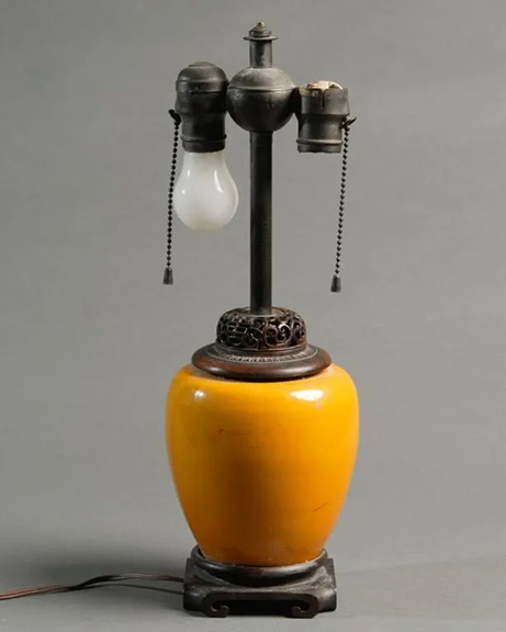 The antique Chinese yellow-orange vase that was converted into a table lamp in the late 19th or early 20th century sold for $475 (est. $100/200). The ovoid vase rests on a rosewood base and is fitted with a reticulated rosewood cap. The two-socket fixture is by Benjamin. The lamp’s overall height is 17
