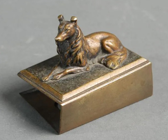 This matchbox cover is topped with an alert but resting dog figure. The underside is marked “Made In Austria.” The figural piece of tobacco memorabilia is slightly out of square and measures 1½