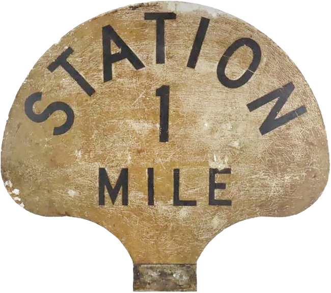 This heavy aluminum sign is likely a railroad marker. Lettered “STATION / 1 / MILE,” the 23