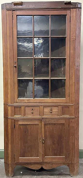 The one-piece Shenandoah Valley, Virginia, corner cupboard is constructed of walnut, with yellow pine as secondary wood. The upper portion features a 12-pane single door that opens to reveal three fixed shelves. The medial portion has two small drawers, and the lower section features two fielded-panel doors enclosing one fixed shelf above the base panel. There is a shaped apron. The front corners are canted and extend to form the feet. There is no cornice, but there remains evidence of applied reeded molding at the waist and below the missing cornice. The 87