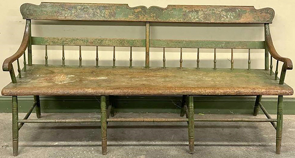 This Windsor-style settee is constructed of poplar and features a shaped, paint-decorated tablet-top back rail. The form is commonly referred to as a deacon’s bench. There are turned spindles supporting the mid-back rail and arms. The settee displays its original green-painted and stenciled surface. The well-worn seat is a single 72