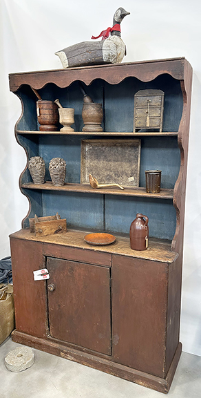 Pewter cupboard, red paint with a blue interior to the open top, with scalloped sides and cornice, sold during the show by Kent and Cheryl Williams Antiques, Pickerington, Ohio. Smalls included a Canada goose decoy, carved wood, $395; mortars and pestles, $125 to $275; a miniature chest of drawers with bootjack feet, the early hardware on the back suggesting it could have been hung or set on a tabletop, $395; two carved wood molds in the form of floral baskets, $495 the pair; a wooden scoop, $110; an apple tray, Amana Colonies, $395; a redware plate, $165; and a quart jug in Albany slip glaze, $135.