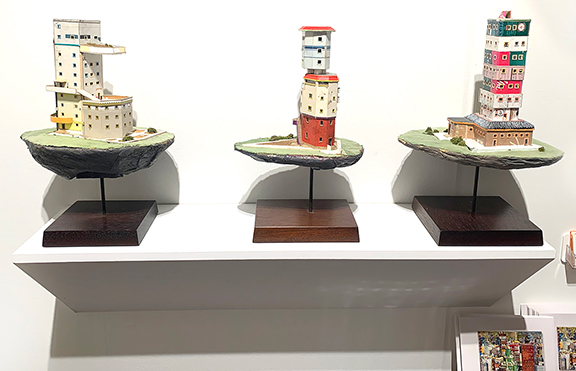 Housing Works, models by Ryder Henry (b. 1974), were available at the booth of Steven S. Powers and Joseph Lowenfels of New York City, priced at $1800 each. The cardboard, paper, and corduroy sculptures are based on “an obsessive scale of 1:213:333,” and Henry places many of them in a city he has built in his home. In the artist’s paintings he adds life, which is absent from the model city.