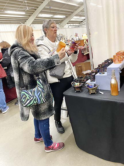 Karen Stoiber of Menomonee Falls, Wisconsin, and Mary Lou Haas of Hartland, Wisconsin, linger over a display of carnival glass at the space of Joe Baran from Arlington Heights, Illinois. The mugs and tumblers were tagged $10 each. 